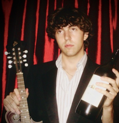 Artist with mandolin and wine before red curtains